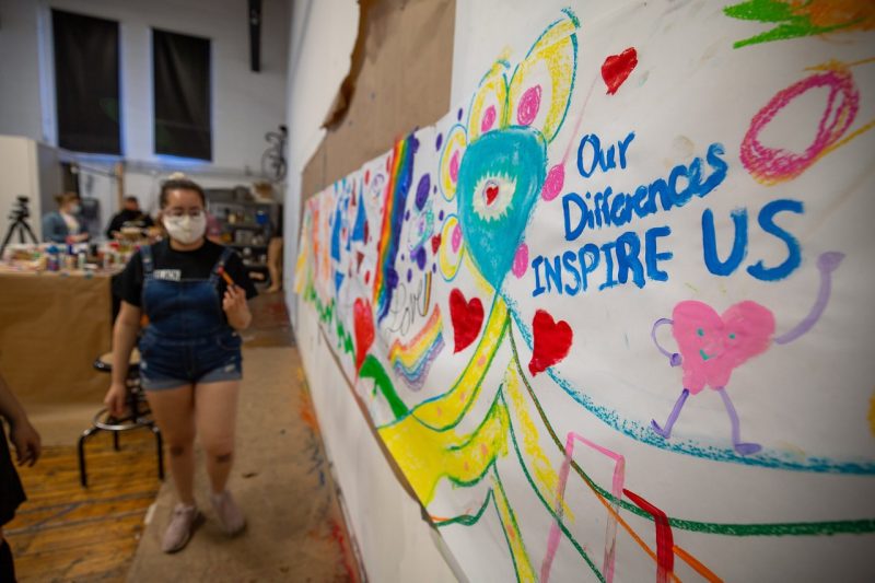 A student walks in the background. In the foreground, the words "Our differences INSPIRE US" are in focus on a painted banner.