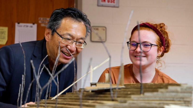 Dean Liu and a student looking at cardboard model on table together