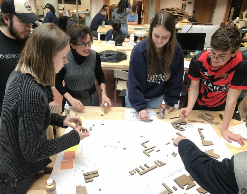Professor and students standing around a table working on a model together.