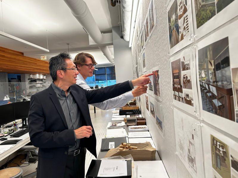 Dean Liu and a faculty member discussing and pointing at work on a wall.