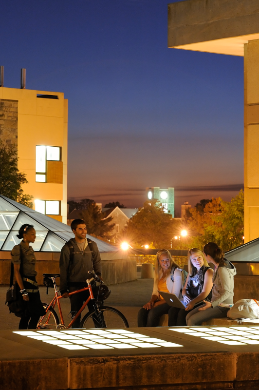 Five students on a campus roof converse under the evening sky.