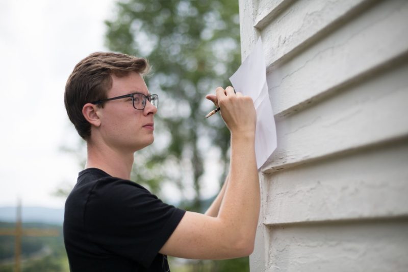 A student carefully sketches on paper braced against an exterior wall.