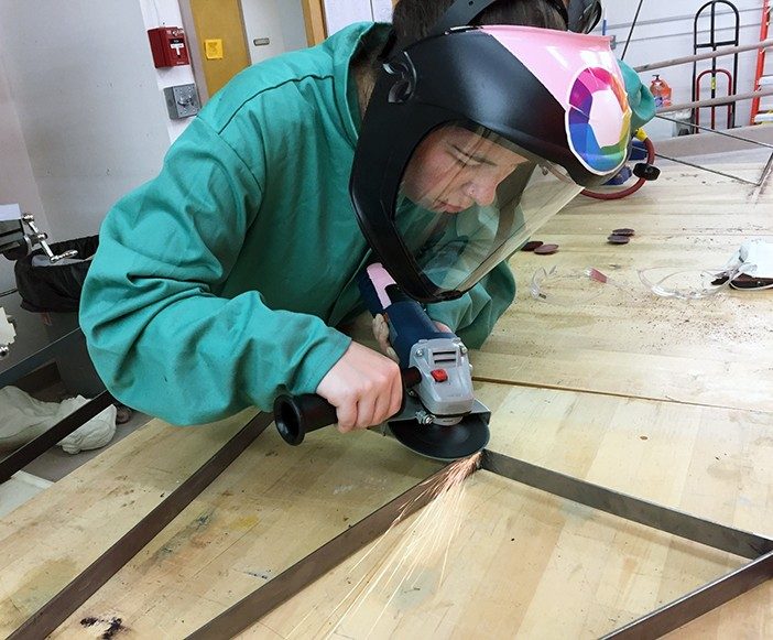 A student in the workshop wears a face shield and operates a grinder.