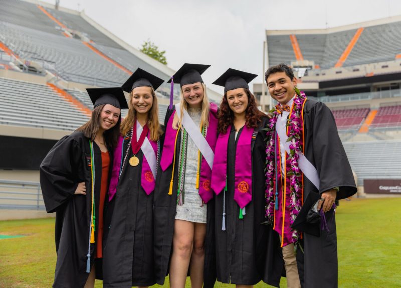 Five students posing together at the commencement ceremony in Lane Stadium.