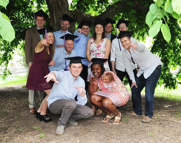 Sheema Laguerre and 10 other graduating students wearing their caps and posing under a tree together.