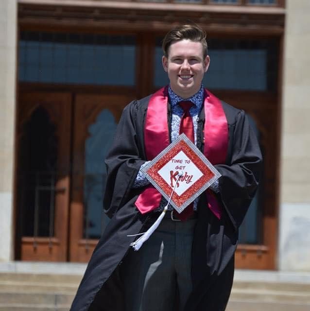 Kevin Foster standing in front of Burruss Hall in graduation regalia, holding his decorated cap.