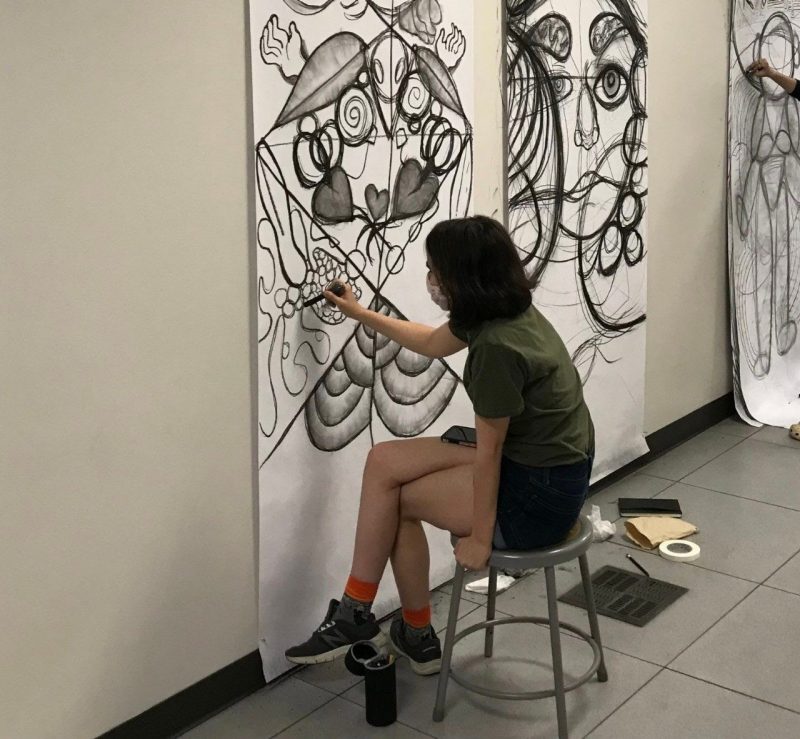 Student drawing on large paper on wall.