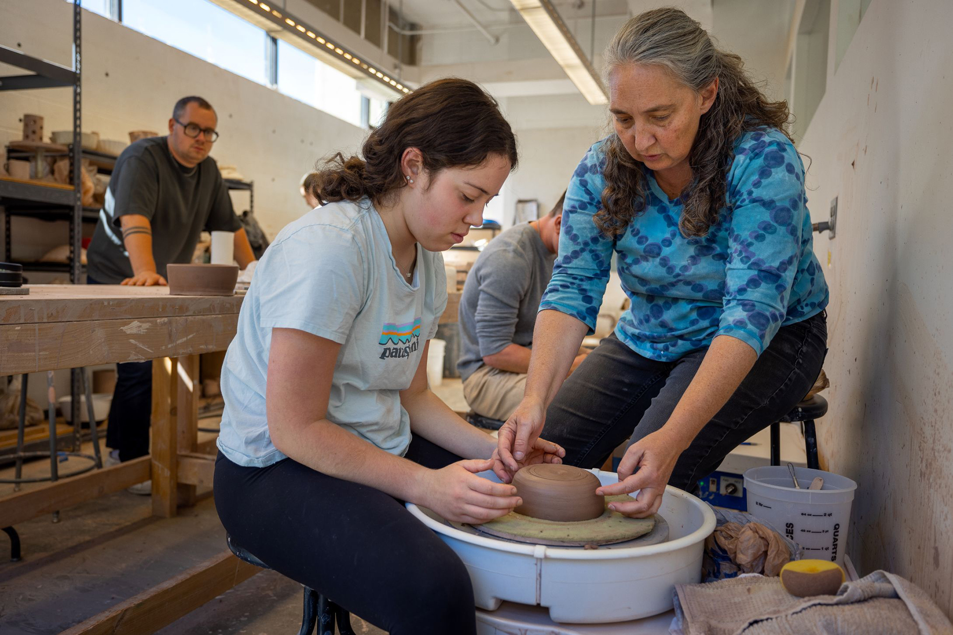 Student learning to make something with clay on the wheel from faculty member.