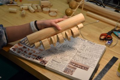 Hand holding wooden prototype with sketches underneath.
