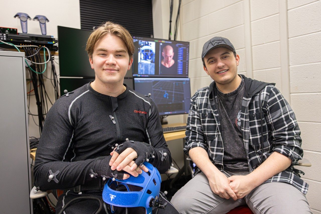 Two creative technologies students sitting together with computer screens behind them.