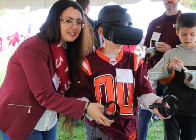 Faculty member shows child how to use VR headset at tailgate.