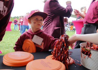 A child holding a frisbee is handed a pompom at tailgate.