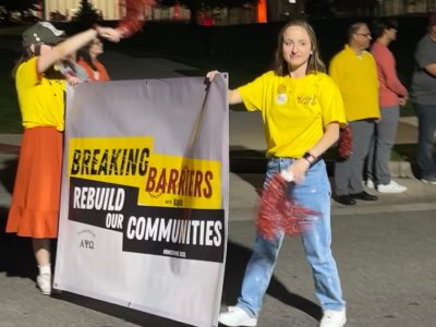 Students at homecoming parade holding up banner that reads, "Breaking Barriers. Rebuild our communities."