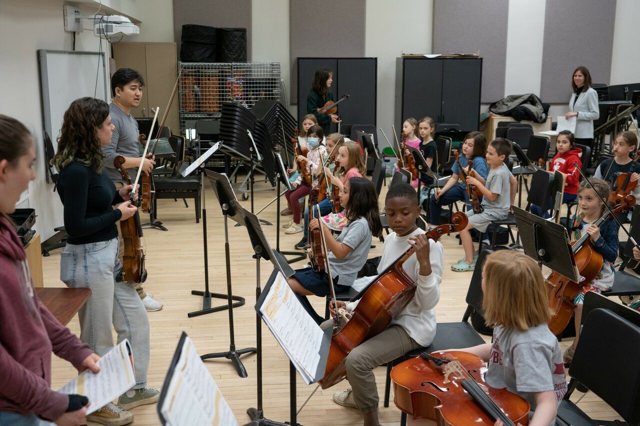 Three music education students teach classroom full of elementary school students holding instruments.