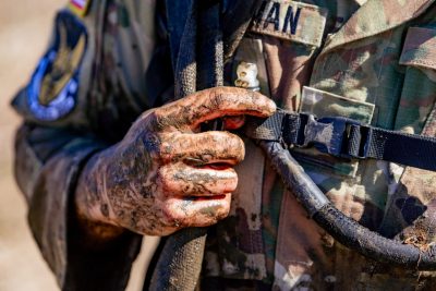  Close-up of a cadet’s arm and hand covered in mud from Platoon Tactical Challenge. The cadet’s uniform and straps are also muddy.