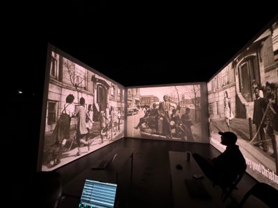 Black background with black and white historical photos displayed in a box shape with a man sitting at a table.
