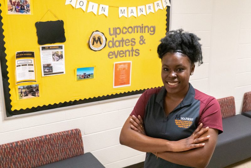 Graduating senior Marquelle Benn stands in front of a MANRRS bulletin board.