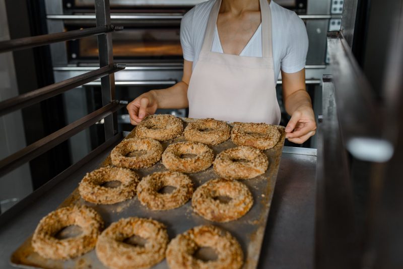 A baker holds a tray with fresh bagels.