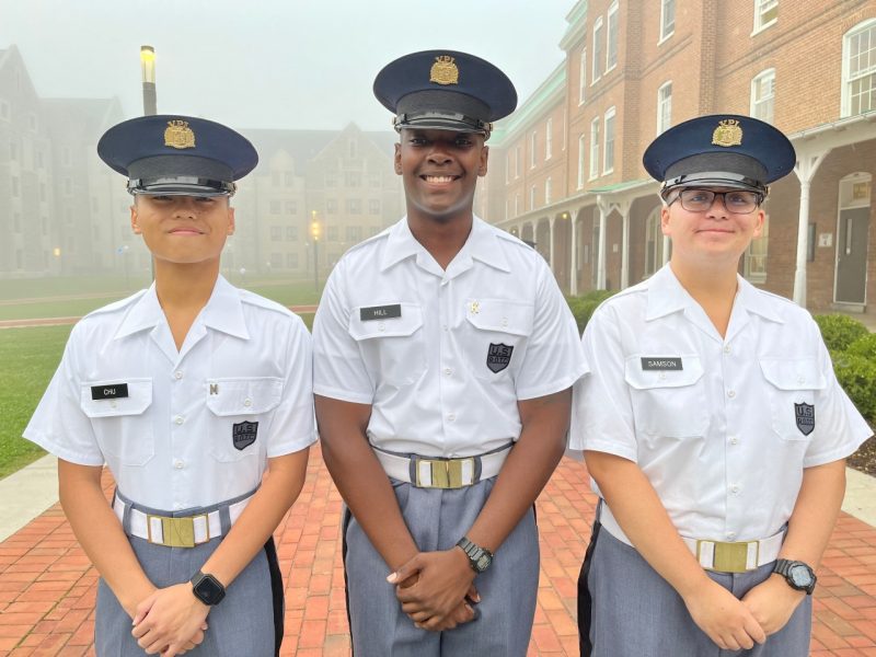Cadets Kevin Chu, Archie Hill, and Nicholas Samson stand in uniform smiling with a heavy fog on Upper Quad in the background.