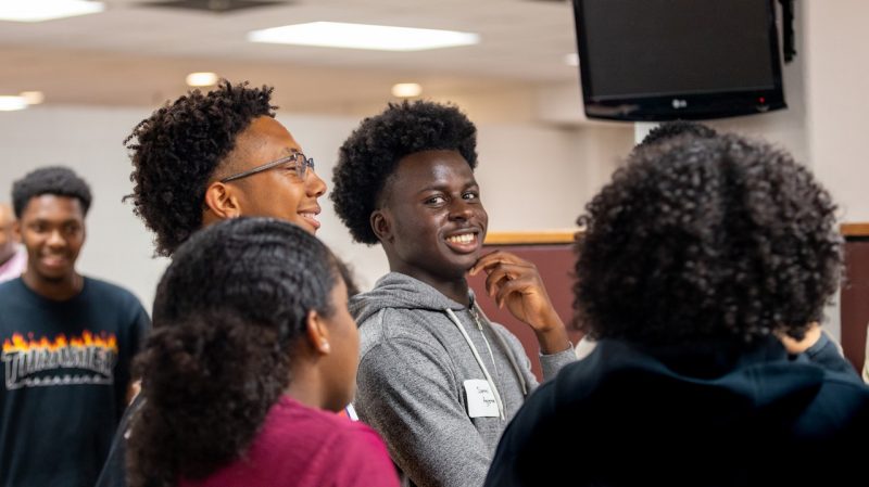 A Black male student in a gray hoodie laughs with several other Black students at a mixer inside the Squires Breakzone at Virginia Tech.