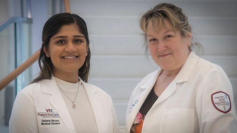 Two women wearing medical white coats smiling at the camera side-by-side